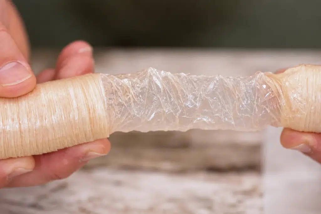 Hands stretching a shirred collagen casing to show its tubular structure